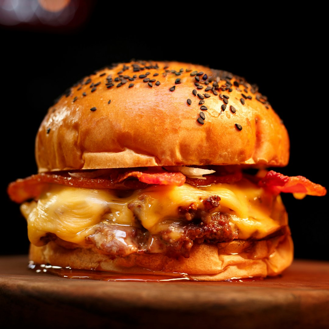 Bacon cheeseburger with melted cheese and black sesame bun on a wooden board.