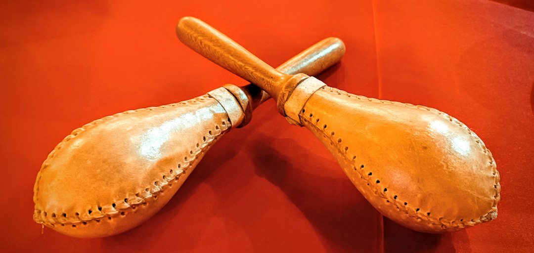 Pair of handmade leather maracas crossed on a red surface.