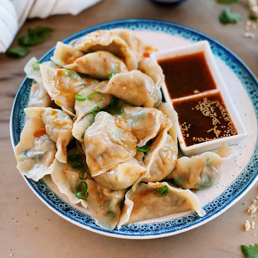 A plate of dumplings with dipping sauce.