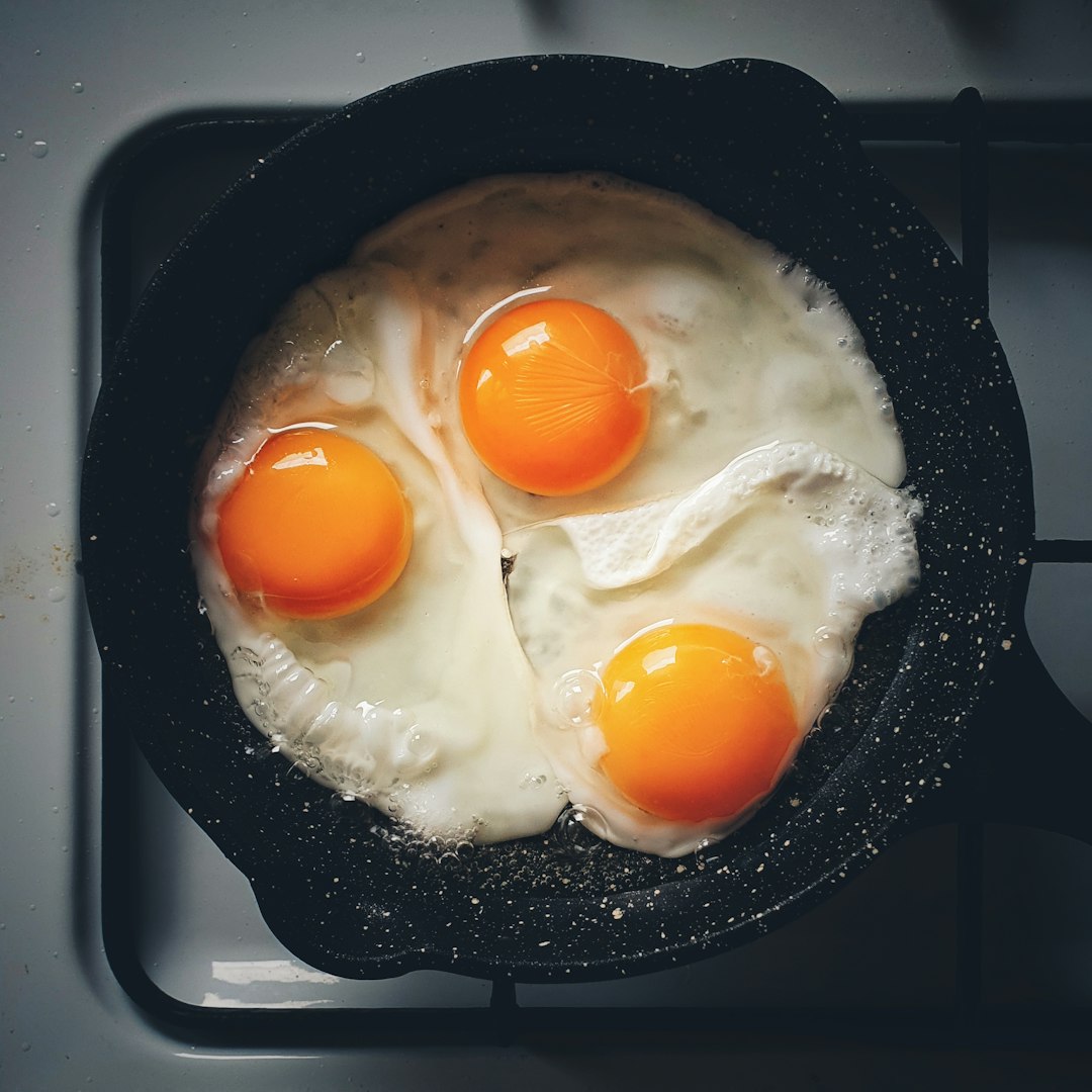 Three fried eggs in a pan on a stove.