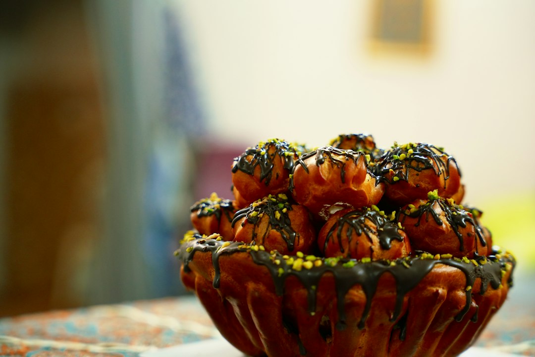 Stack of profiteroles in a fluted pastry bowl, drizzled with chocolate and sprinkled with crushed pistachios.