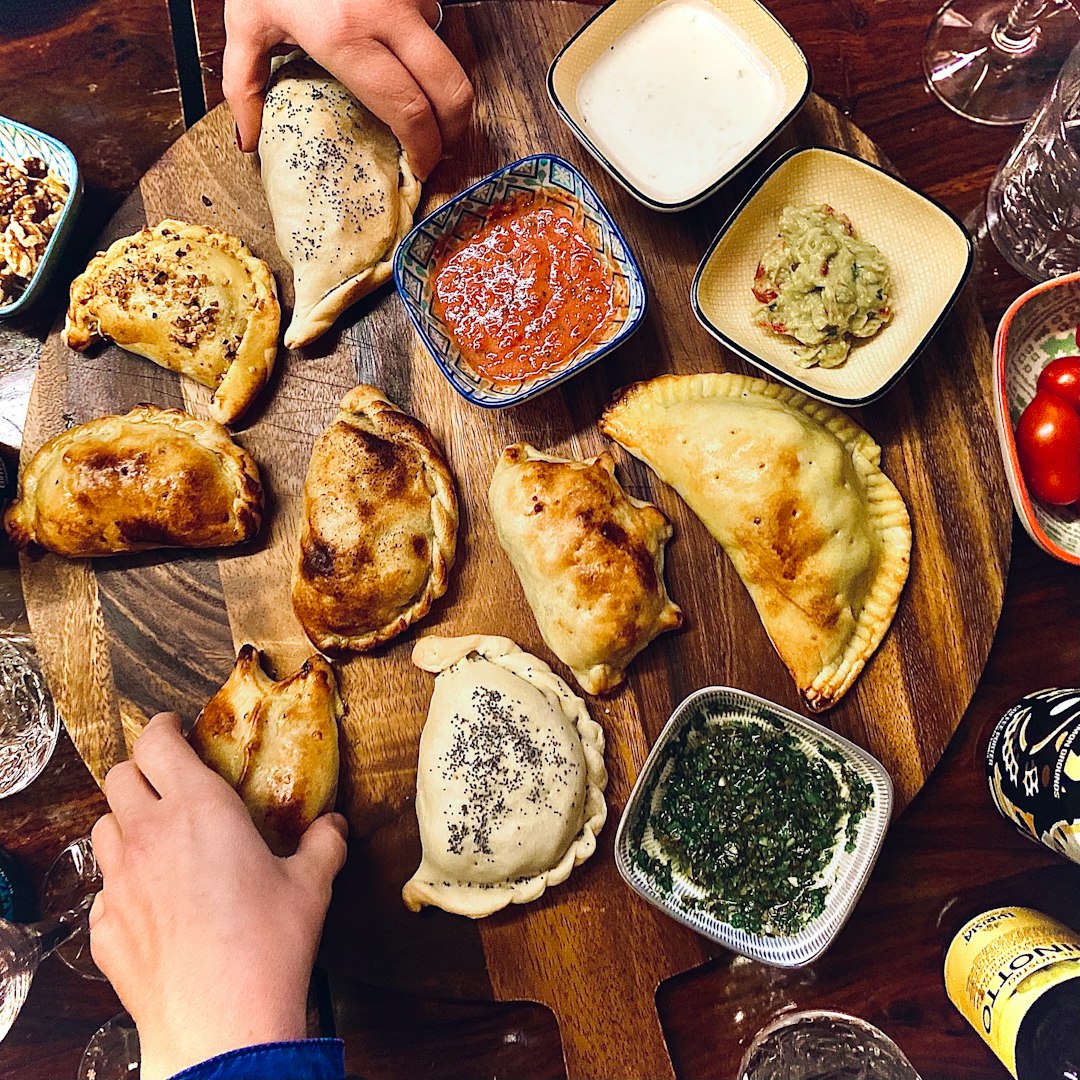 Variety of empanadas on a wooden board with dipping sauces.