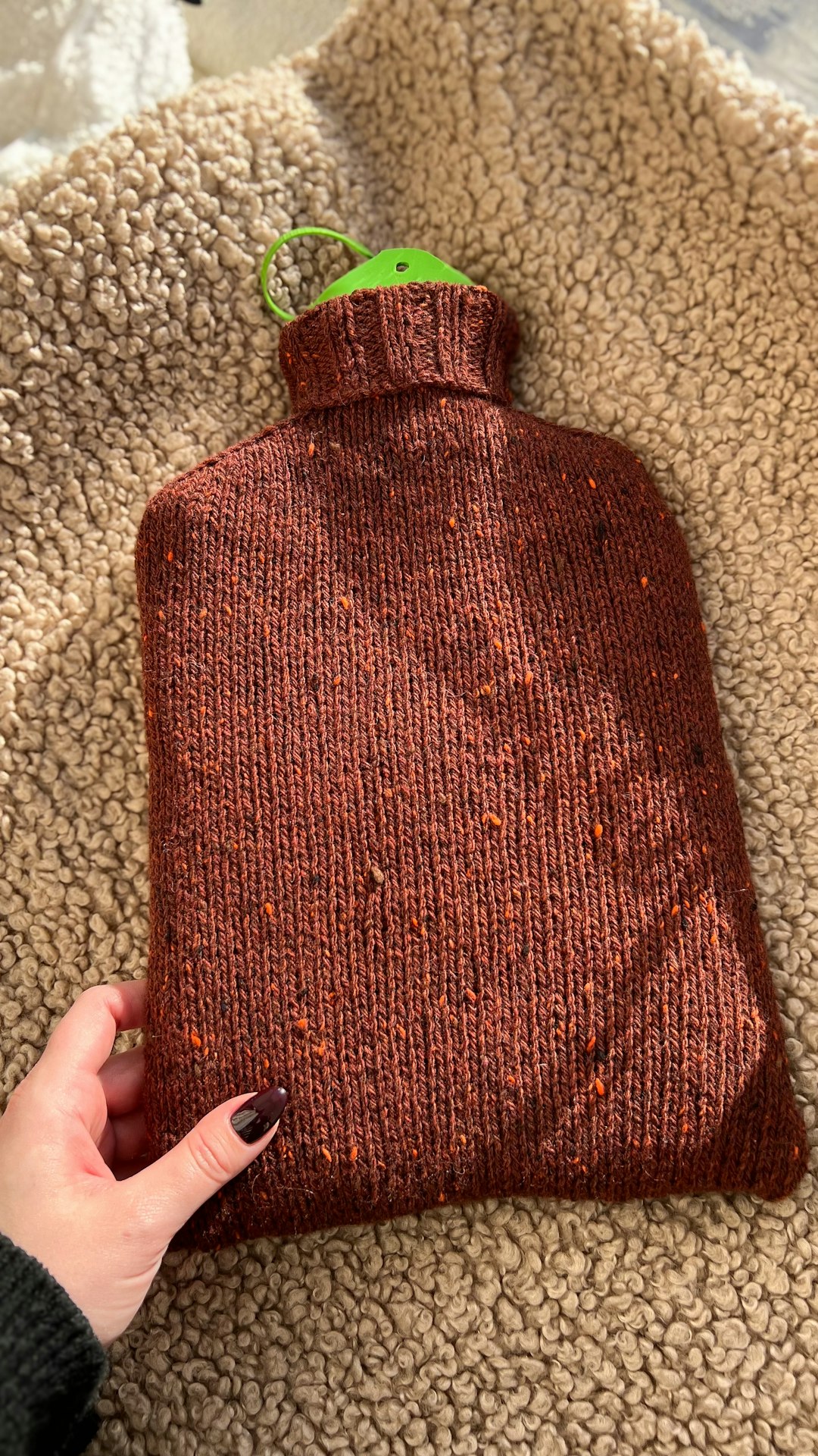 Knitted hot water bottle with a green stopper.