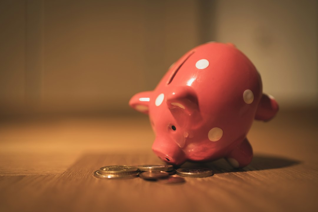 A pink polka-dot piggy bank nosing a small pile of coins.