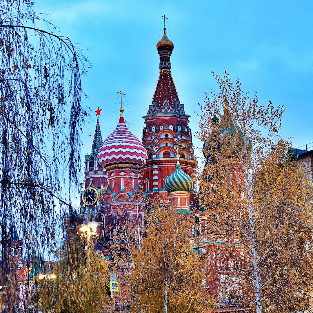 St. Basil's Cathedral, Moscow, its onion domes rising above autumn trees against a blue sky.